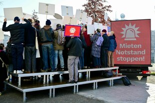 Eine Gruppe von Aktivisten hält Schilder hoch, die nur von hinten zu sehen sind, daneben ein Transparent auf einem LKW: Mieten Notstand stoppen