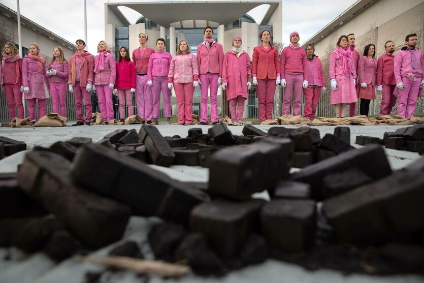 Eine Menschenreihe in Pink gekleidet steht hinter einem Haufen Kohlebriketts