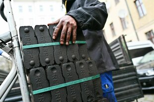 Die Hand eines Kohlenträgers liegt auf einem Paket mit Steinkohle, das auf einer Sackkarre steht