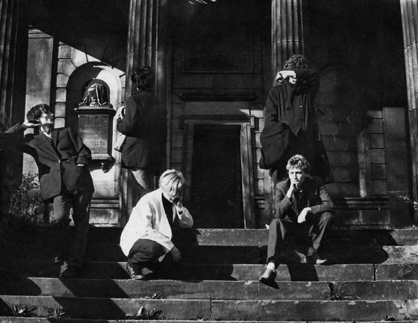 Die Musiker von Clock DVA stehen und sitzen auf den Treppenstufen vor einer Kirche