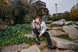 Der Rapper Baran Kok sitzt auf Steinen in einem Park