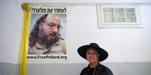 Eine Frau mit Hut steht neben einem Plakat des Spions Jonathan Pollard, das mit gelben Stoffbändern geschmückt ist
