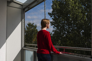 Die Protagonistin Anna Krause steht an einem geöffneten Fenster von hinten fotografiert
