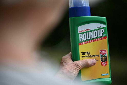 Eine Frau hält in ihrem Garten eine Flasche des Unkrautvernichters Roundup in der Hand