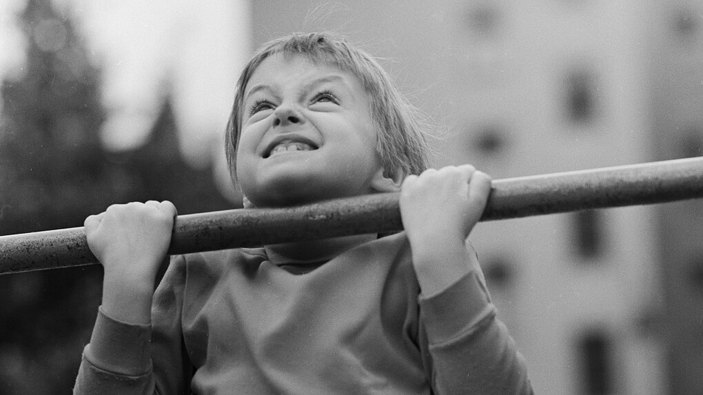 Schwarz-weiß-Aufnahme von einem kleinen Jungen, der Klimmzüge macht