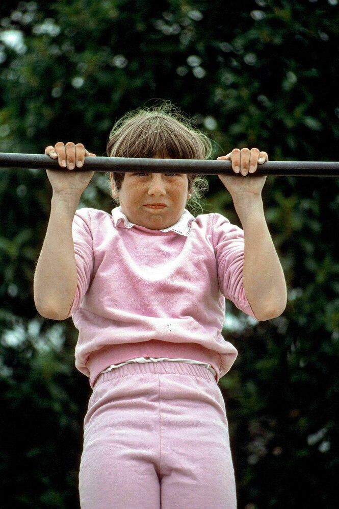 Ein Mädchen in einem rosafarbenen Traingsanzug versucht einen Klimmzug zu machen