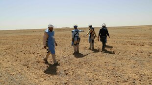 Vier Männer in Schutzkleidung in einer Wüstenlandschaft