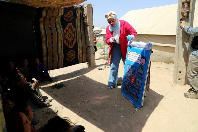 Die Lehrein Yeter steht vor einer Hütte und dseutet auf eine Schautafel