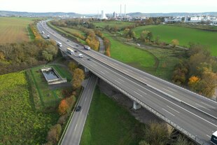 Kaum befahrene sechspurige Autobahn zieht sich durch die Landschaft, im Hintergrund Industrie