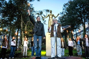 Eine junge Frau und Dunya Verweij und stehen vor der Statue von Wilhelmina Drucker - die Frauen hinter ihnen im Halbkreis recken ihre brennenden Fackeln in die Höhe