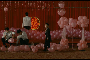 Ein Junge (Jonathan Chang) zwischen lauter rosa Luftballons, die Kellner festlich arrangieren.