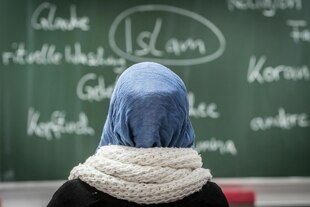Eine Person mit Kopftuch schaut auf eine Schultafel