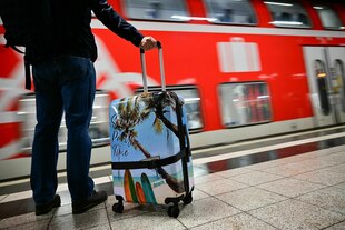 Eine Person steht mit Reisekoffer an einem Bahngleis