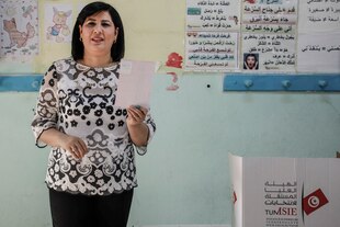 Abir Moussi hält mit ihrer Hand einen Stimmzettel in die Höhe, sie steht in einem Raum neben einer Wahlurne.