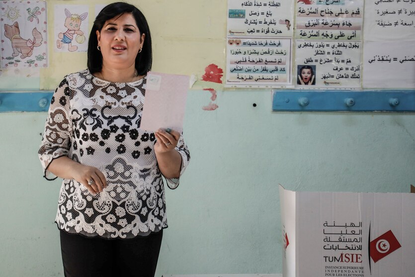 Abir Moussi hält mit ihrer Hand einen Stimmzettel in die Höhe, sie steht in einem Raum neben einer Wahlurne.