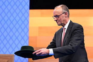 Friedrich Merz legt einen dunkelgrünen Trachtenhut neben sich ab