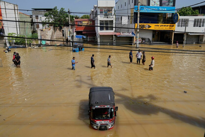 Menschen waten durch kniehohes, braunes Wasser, eine Autorikscha steht bis zur Motorhaube im Wasser
