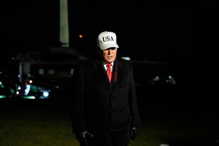 Donald Trump trägt ein weißes USA-Käppi, es ist Nacht.