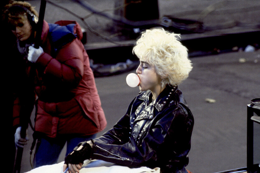 Madonna macht eine Kaugummiblase, hinter ihr steht eine Frau mit einem Filmmikrofon