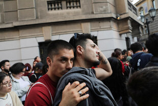 Zwei Männer stehen auf einer Straße, einer lehnt seinen Kopf an des anderen Schulter von hinten