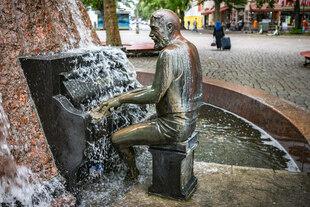 Die Skulptur eines Klavierspielers in einem Brunnen auf einem Platz