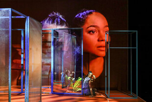 Schauspielerinnen auf der Bühne zwischen Glaswänden. Auf den Bühnenhintergrund ist ein weitere Frauenkopf projiziert