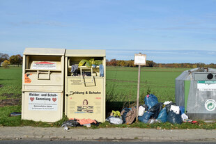 Container für alte Kleider vor grüner Wiese und blauem Himmel.