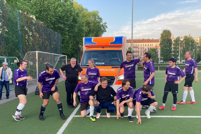 Gruppenfoto des Panter FC auf einem Kunstransenplatz, im Hintergrund ein Rettungswagen