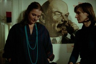 Charlotte Matthiesen lehnt an der Wand, neben ihr ein überlebensgroßer Lenin-Kopf auf einem Plakat, ihr gegenüber Angelika Rommel