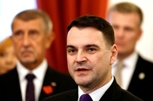 Männer in schwarzen Anzügen stehen vor einem roten Vorhang.