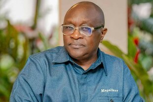 Ein schwarzer Mann in blauem Hemd mit Glatze und klassischer Brille blickt ruhig in die Kamera