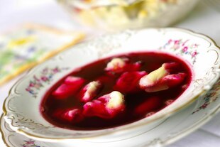 Ein Teller mit klarer Rote-Bete-Suppe und Teigtaschen auf einem festlich gedeckten Tisch