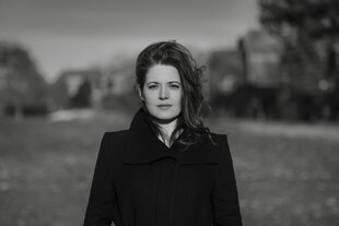 Porträt der Autorin Juliane Baldy - sie hat lange dunkle Haare und trägt einen schwarzen Mantel