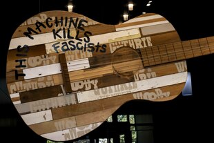 Übergroße Darstellung einer Gitarre aus unterschiedlichen Holzdielen auf welcher "This machine kills fascists" zu lesen ist