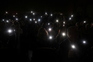 Menschen halten ihre Smartphones in die Höhe, die Lampen der Geräte strahlen in der Dunkelheit