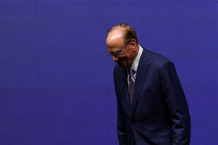 Larry Fink leicht nach vorne gebeugt, mit Brille in einem klassischen schwarzen Anzug, kaum erkennbar vor einer blauen Wand