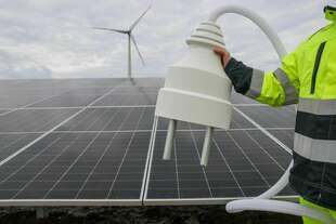 Ein Mitarbeiter von Statkraft wartet mit einem überdimensionalen Stecker vor einer Solaranlage und einem Windkraftwerk