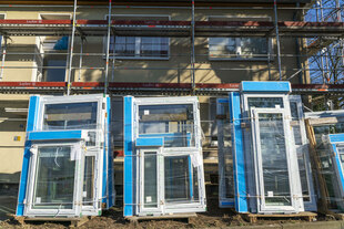 Älteres Mehrfamilienhaus ist eingerüstet, neue Fenster lehnen aneinander vor dem Gerüst