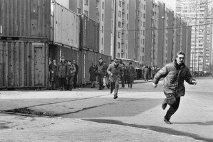 Schwarz-weiße Aufnahme einer Straße, auf der zwei Menschen rennen. Im Hintergrund Hochhäuser
