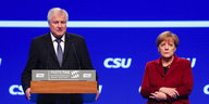 Horst Seehofer tront an seinem Rednerpult, Frau Merkel steht bedröppelt daneben