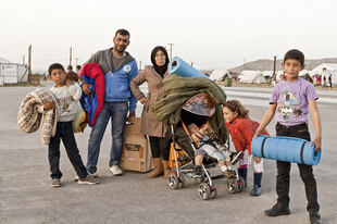 Eine geflüchtete Familie mit ihrem Gepäck, Isomatten und Decken