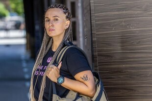 Eine Frau mit geflochtenen Zöpfen und Kargohose blickt in die Kamera