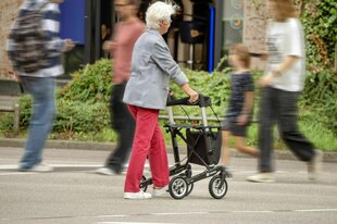 Unterwegs mit dem Rollator - eine ältere Frau in der Stadt, jüngere Leute gehen an ihr vorbei -