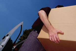 Detailansicht, die Arme eines Mannes der ein Paket schleppt vor blauem Himmel und einer geöffneten Autotür