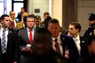 US-„Kriegsminister“ Pete Hegseth, umringt von einem Beamtentross, mit Kaffeebecher in der Hand