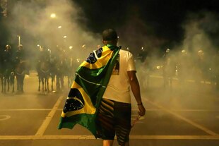 Ein Anhänger des Ex-Präsidenten Bolsonaro mit Brasilienflagge um die Schultern, stellt sich gegen eine Reihe berittener Polizisten