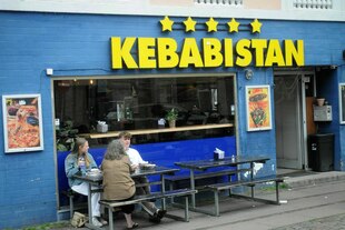 vor einem Kebabladen in Kopenhagen sitzen Menschen und essen - der Name des Ladens - Kebabistan - steht in großen Buchstaben an der Fassade