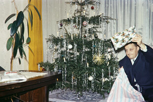 Mann mit Geschenk und Topfplanze neben dem Weihnachtsbaum um 1950