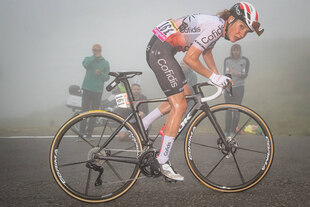 Radprofi Klara Koppenberg beim Bergauffahren in nebliger Umgebung schaut in die Kamera.
