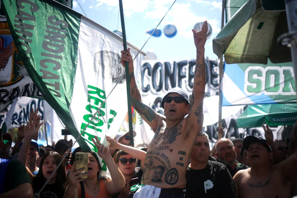 Protest in Bueonos Aires - die Menschenmenge schwenkt Fahnen der Gewerkschaften, im Mittelpunkt ein tätowierter Mann der die Arme in die Höhe reckt